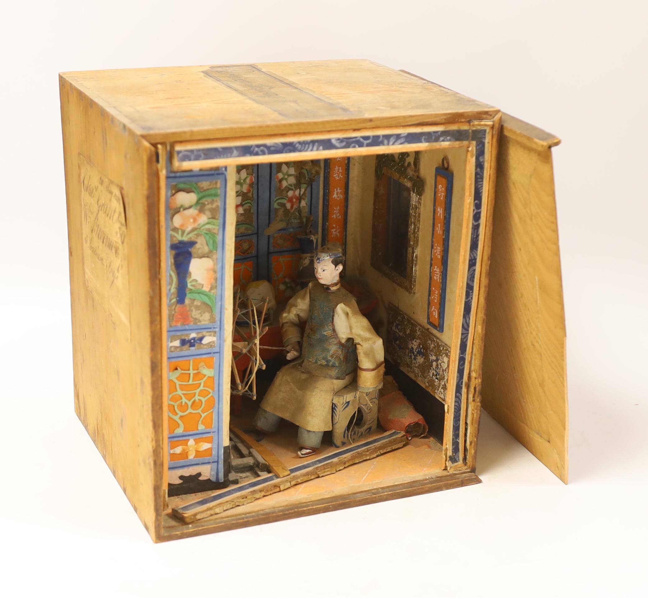 A Chinese card, paper and silk diorama depicting a seated artisan at a spinning wheel, 19th century, (label to the side of box) 22cm wide x 24.5 cm high